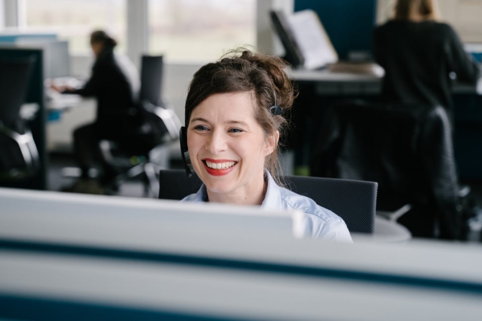 Eine Mitarbeiterin mit einem Headset sitzt in einem Callcenter und führt ein Telefonat