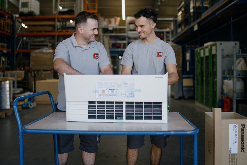 Zwei RGS-Mitarbeiter mit einem neuen Klimagerät im Lager in Ingolstadt